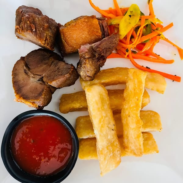 Salvadoran dish with fried yuca, beef, curtido, and a side of red sauce on a white plate.