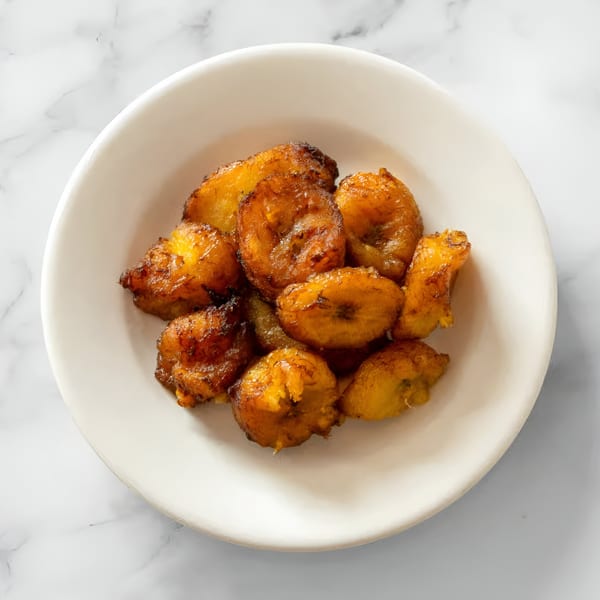 A white bowl filled with golden-brown fried plantains, a traditional Salvadoran side dish.