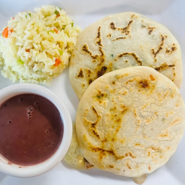 Two pupusas, a side of white rice with vegetables, and a small bowl of dark bean dip.