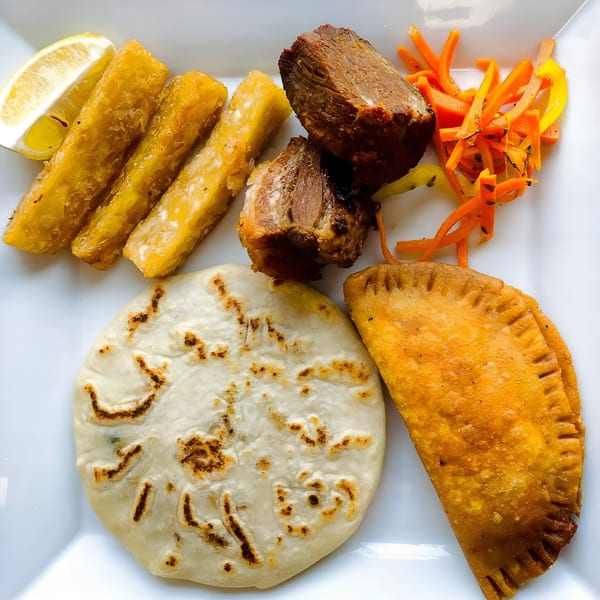 A Salvadoran platter with fried yucca, pupusa, empanada, seasoned pork, and pickled vegetables.