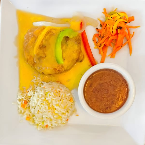 Salvadoran dish with chicken in yellow sauce, white rice, shredded carrots, and a side of brown sauce.